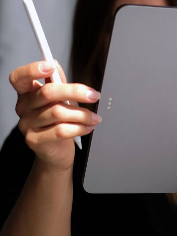 A hand holding a stylus, positioned near a mobile phone on a surface